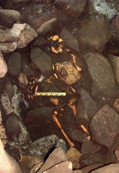 Photo of the remains of a human skeleton among stones in a cave.