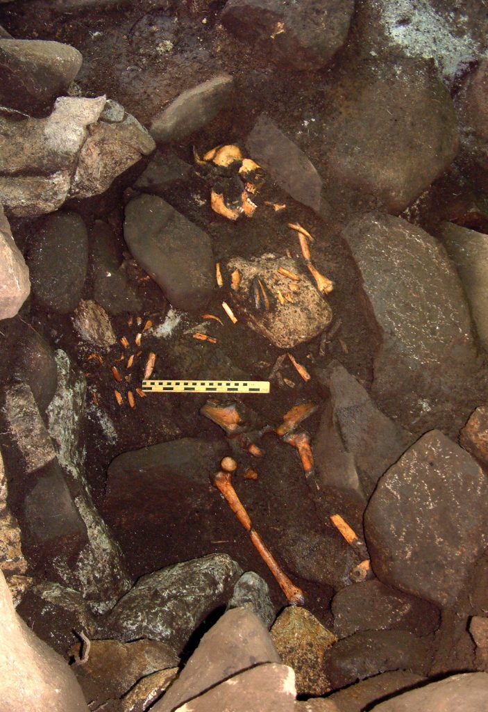 Photo of the remains of a human skeleton among stones in a cave.