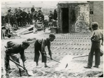 [IMAGE 6: Boys preparing pig iron moulds in a bed of casting sand at Coltness Iron Works, Newmains around 1910. In the background the men of the furnace team wait to ‘tap’ the blast furnace.]
