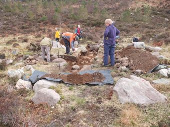 Photo of a group of people standing around an archaeological trench.