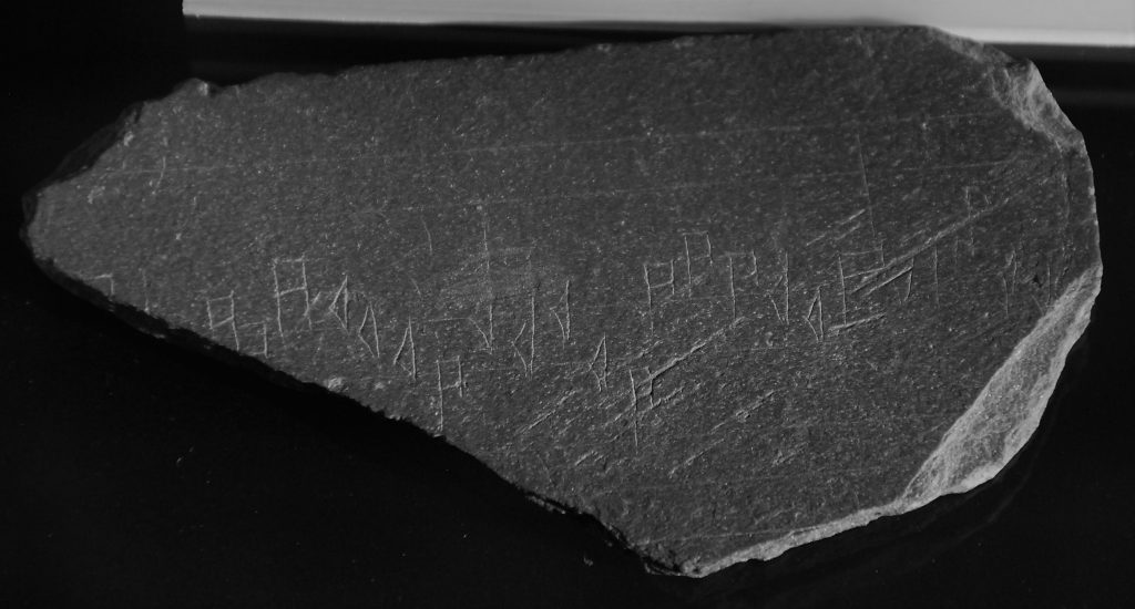 Photo of a triangular piece of slate with musical notations scratched on it.