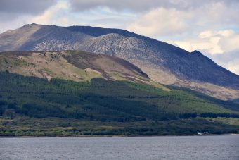 Photo of large grey mountains on an island with water in the foreground.