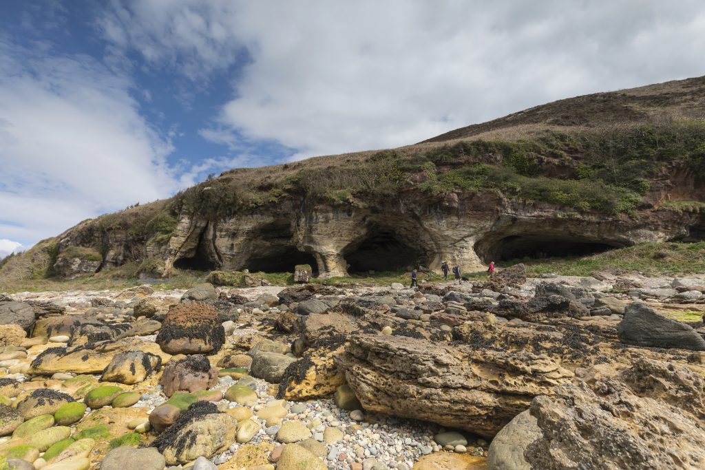 Photo of a series of chambered caves along a pebble beach.