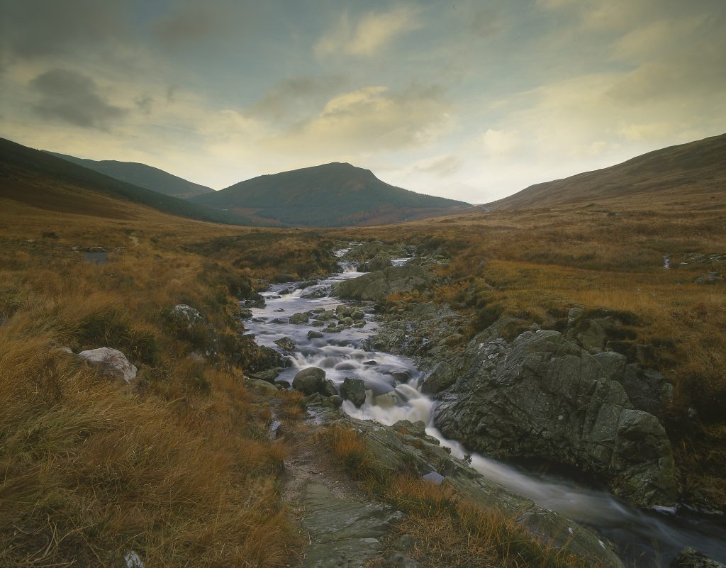 Photo of a stream running in a glen at twilight with hills in the background