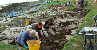 People digging around stone with water in the background
