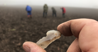 Someone holding up a flaked stone on a field with people in the background
