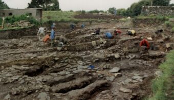 Photo of a dozen people working in a huge archaeological trench in an old graveyard