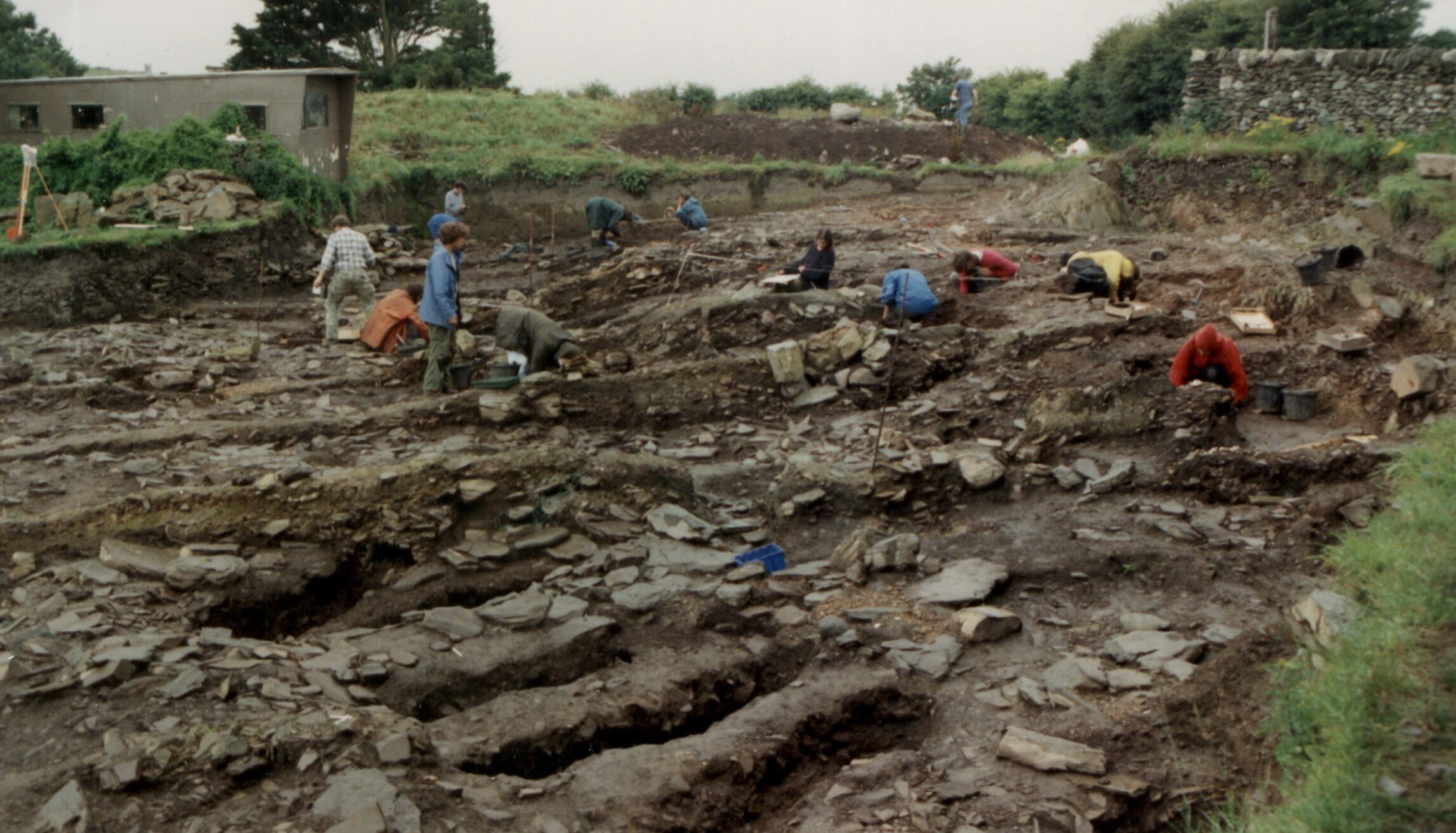 Photo of a dozen people working in a huge archaeological trench in an old graveyard
