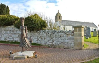 Photo of the statue of a woman with a tall hat in medieval clothing outside a church