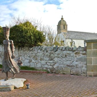 Photo of the statue of a woman with a tall hat in medieval clothing outside a church
