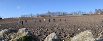 Several people walking in a line in a field - boulders in the foreground