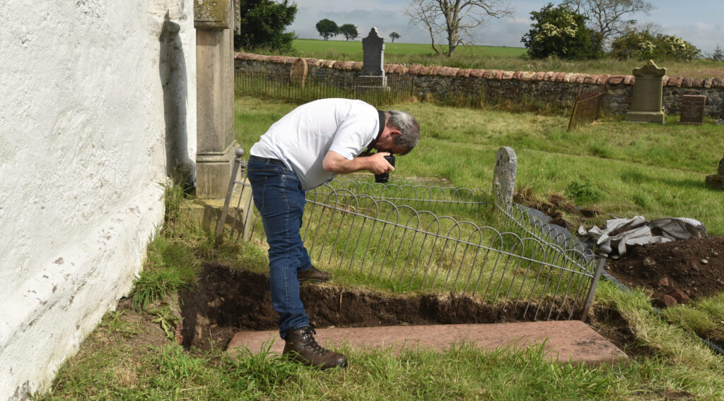 A man taking a photo of an excavated grave slab
