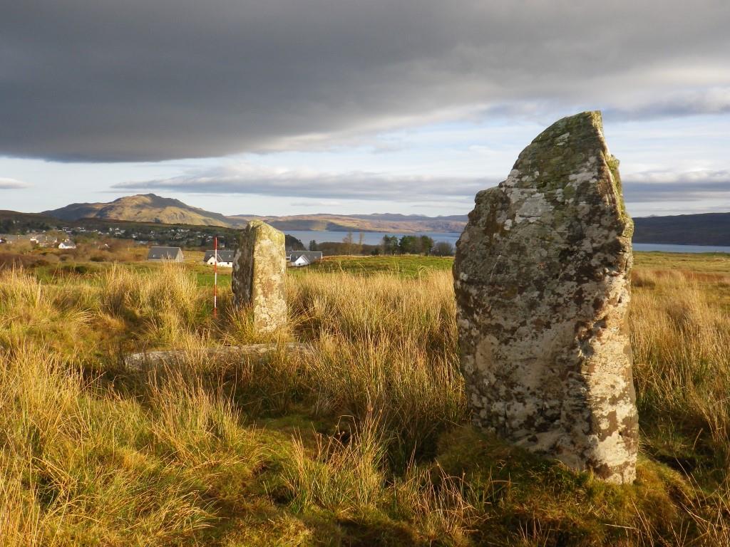 Photo of two short standing stones in a row on an island with mountains in the background