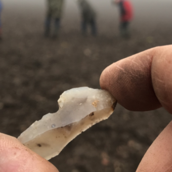 Someone holding up a flaked stone on a field with people in the background