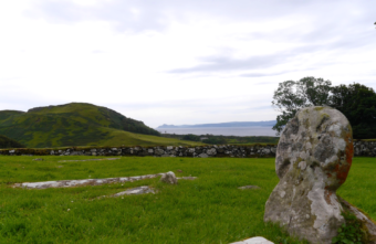 Photo of the remains of a stone structure and a standing stone in a field