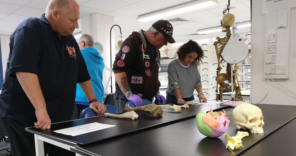 Photo of four people in a lab, looking at human bones on a table.