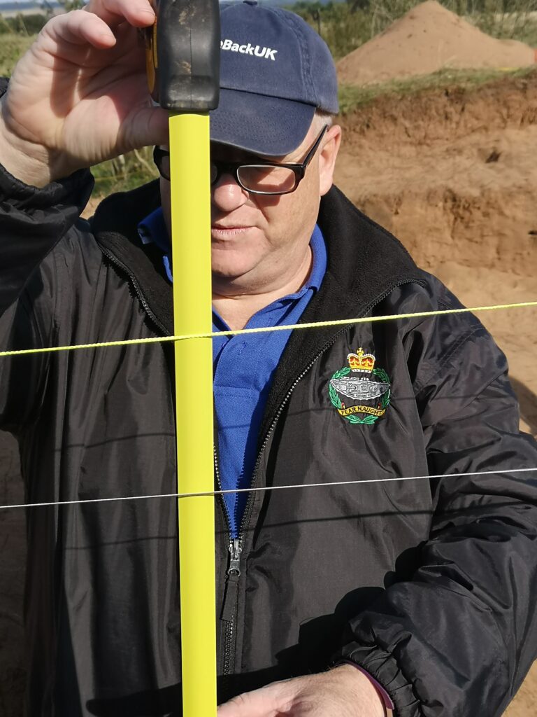 Photo of a man in a black waterproof jacket and a black cap measuring a distance with a tape measure.