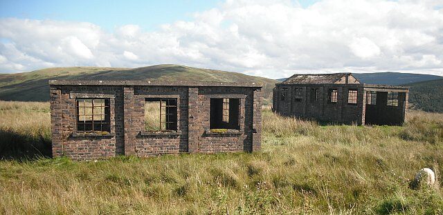Two abandoned stone buildings in a field - hills in the background