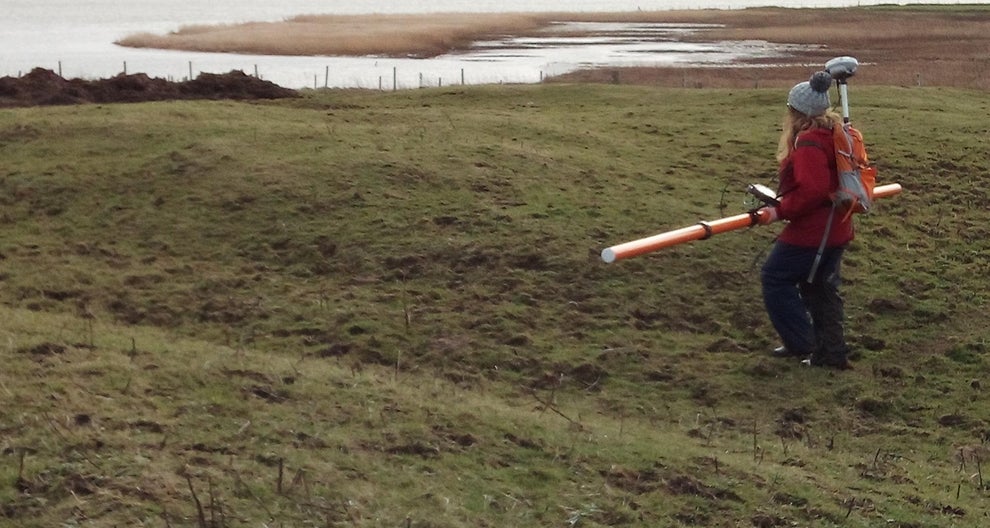 Person walking across a field carrying equipment