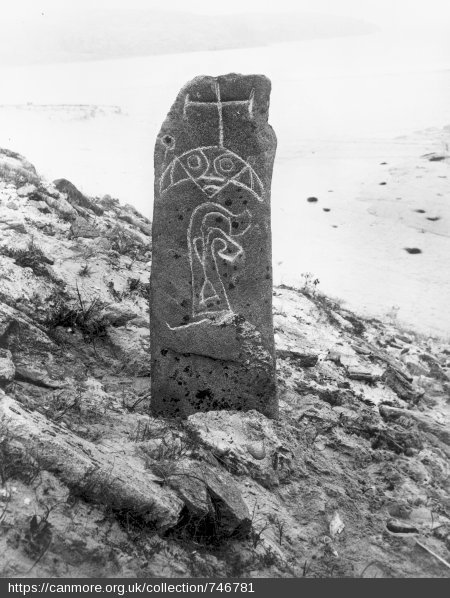 Black and white photo of a tall, carved standing stone covered in symbols