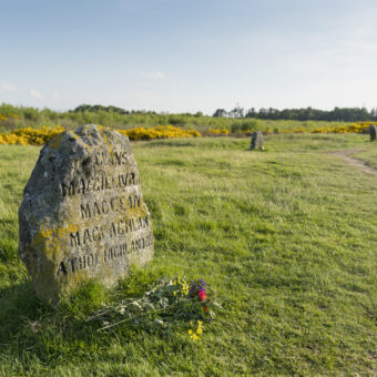 Photo of a small stone memorial commemorating fallen soldiers from three Highland clans, with further stones visible in the background