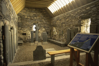Photo of the interior of a small stone chapel showing carved standing stones on display and an information board