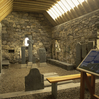 Photo of the interior of a small stone chapel showing carved standing stones on display and an information board