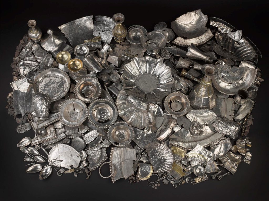 Photo of a huge hoard of hacked ancient Roman silver, including dishes, plates, vases and cutlery, laid out on a black background
