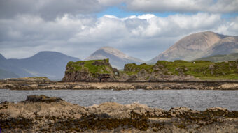 Photo of a ruined stone castle by the sea with huge mountains in the background