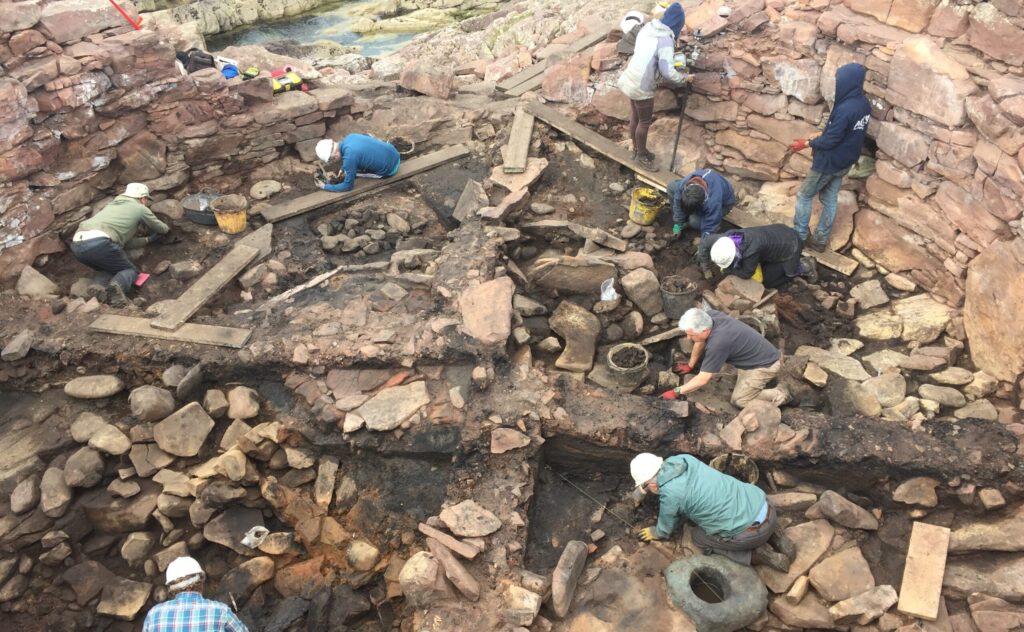 Photo of the stone remains of a large building being excavated by 6 people