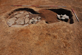 Photo of a partially excavated Roman bread oven with stones lining the bottom