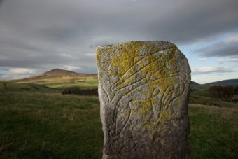 Photo of a carved Pictish stone with a mountain in the background