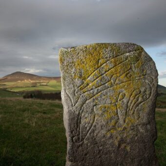 Photo of a carved Pictish stone with a mountain in the background