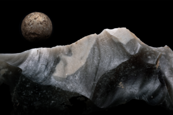 Piece of flint in front of a lead shot on a black background resembling a lunar landscape