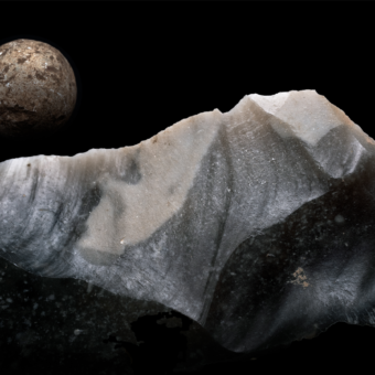 Piece of flint in front of a lead shot on a black background resembling a lunar landscape