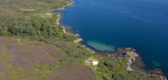 Aerial view of a large stretch of water and the coast - a small campsite can be seen