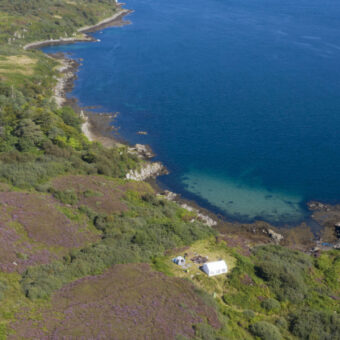 Aerial view of a large stretch of water and the coast - a small campsite can be seen