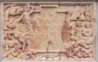 Photo of a carved stone slab with Latin lettering, human figures and horses