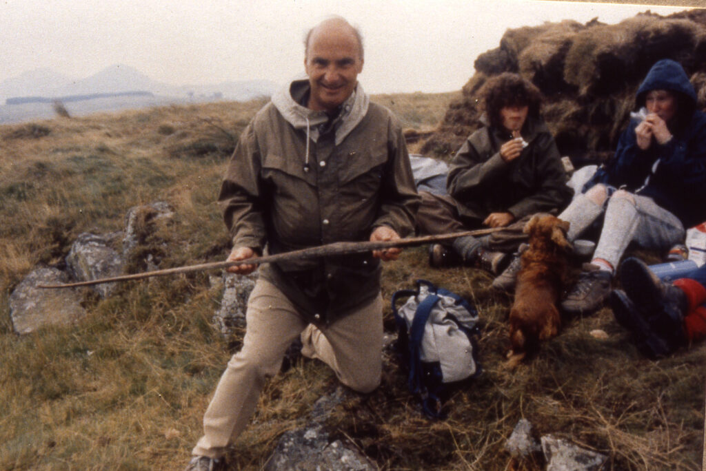 Photo of a man in waterproof clothing holding a long thin, broken wooden bow