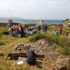 Several people standing around an archaeological site with stone ruins in the background by the water