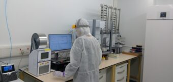 Photo of a person in white lab overalls and mask working in a lab