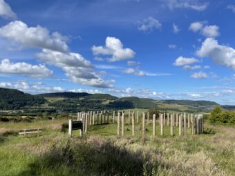 Photo of a reconstructed hillfort boundary in a field with hills in the background