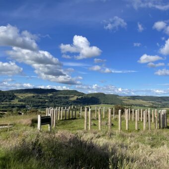 Photo of a reconstructed hillfort boundary in a field with hills in the background