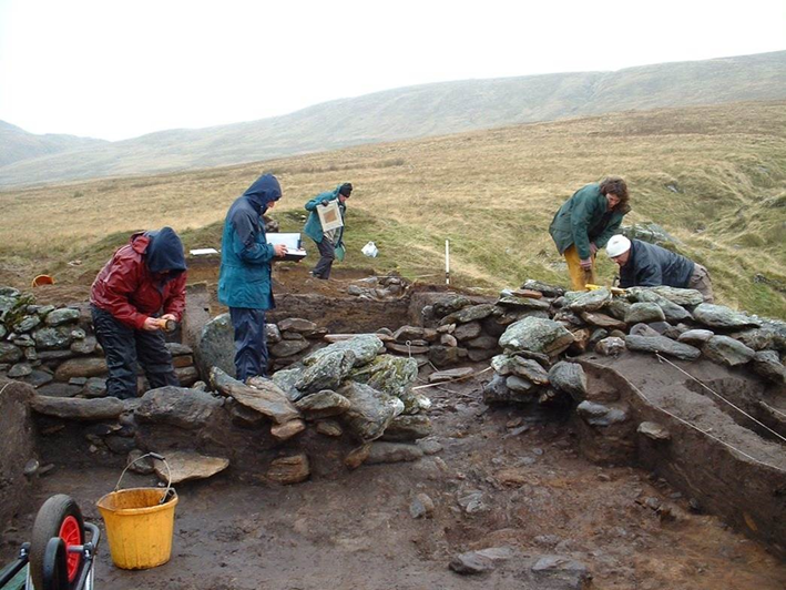 Photo of four people in waterproof clothing digging at an archaeological site