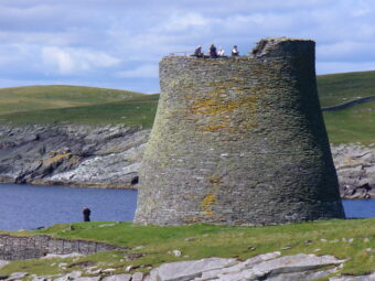 Photo of a large stone roundtower on the edge of an island with people at the top