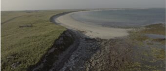 Photo of an eroding settlement mound in a bay by the sea