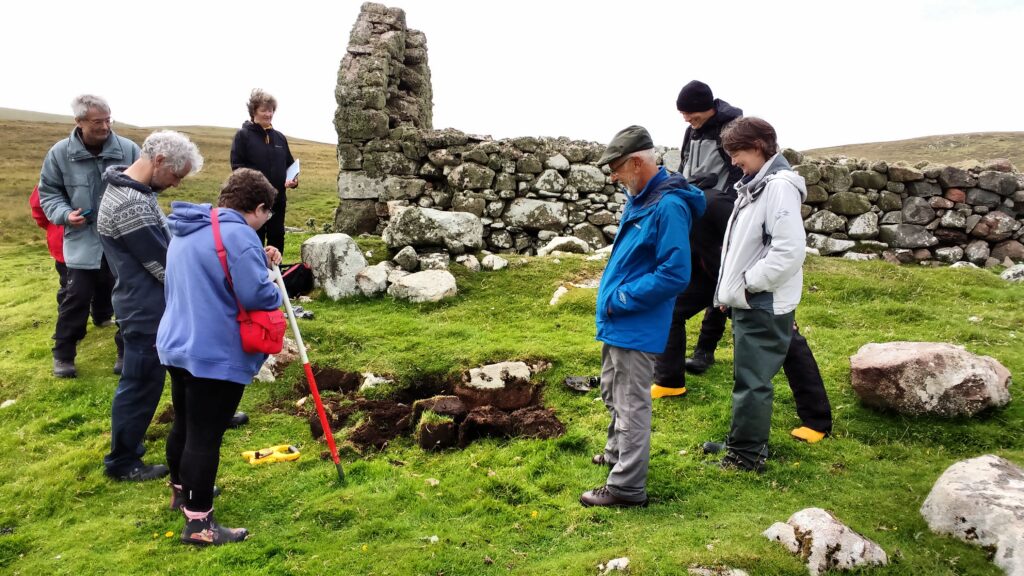 Several people standing around a test pit beside the stone structure