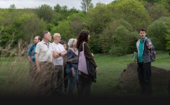 People in a grassy environment listening to a guide