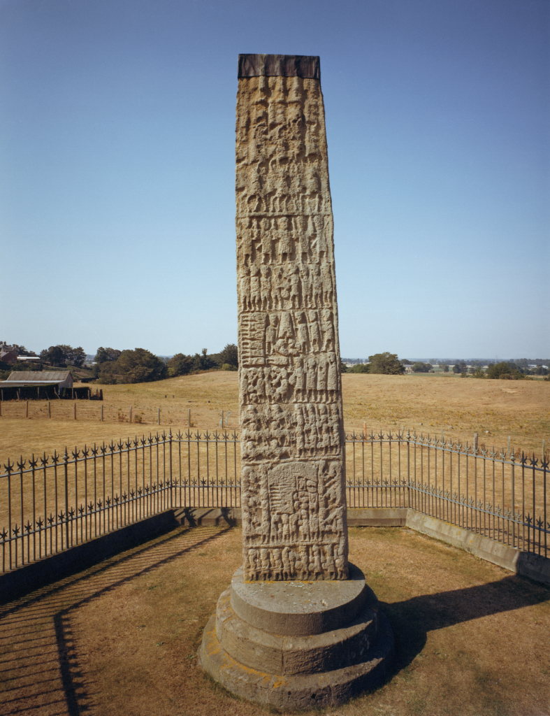 Photo of a tall carved stone slab packed with small carvings of several scenes involving humans