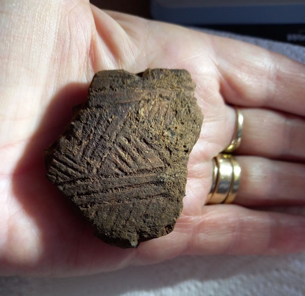 A palm-sized piece of decorated brown pottery held up to the camera in a person’s hand 